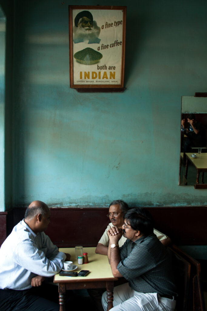Three Indian gentlemen engage in conversation at a local café, photo by Parikshit Rao.