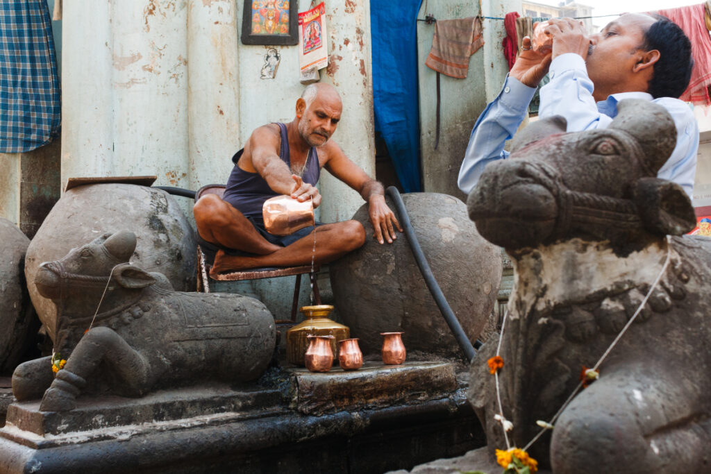 Two men enjoy traditional beverages from copper cups on the streets of India, image by Parikshit Rao.