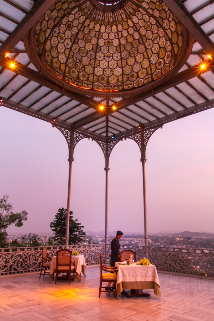 As the sun begins to set, the majestic Taj Falaknuma Palace stands tall, casting a mesmerizing glow against the evening sky, showcasing the timeless beauty and grandeur of Hyderabad's architectural heritage.