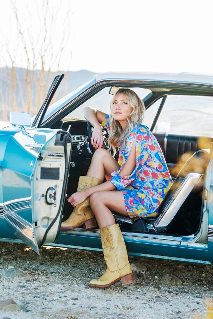 Woman sitting in a car wearing colorful clothes and cowboy boots, photographer by Paula Watts.