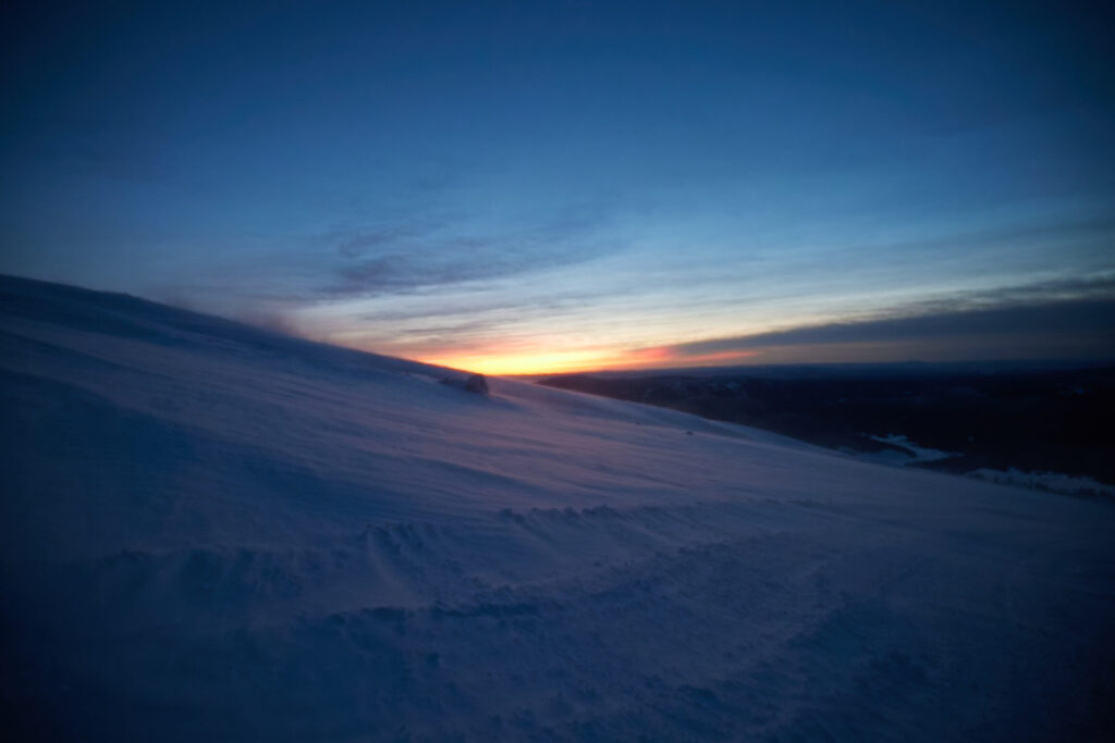 Image of a sun setting behind a snowy hill.