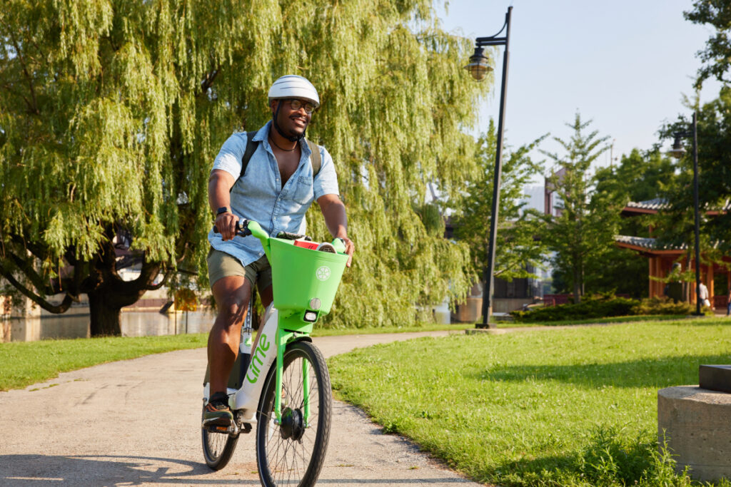 An image of a man joyfully navigating through a verdant park astride a Lime bike, photo by Ricky Klüge.
