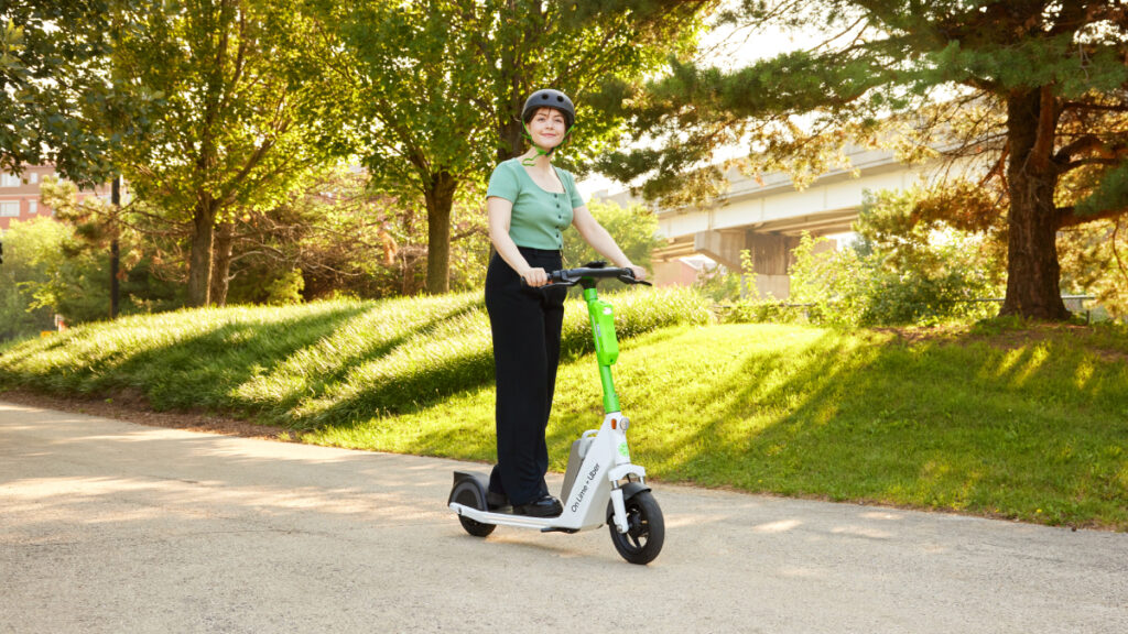 Image of a woman riding through a lush green park on Lime's electric scooter.