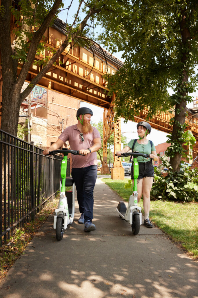 A man and woman stroll beside their Lime scooters, the sleek electric vehicles blending seamlessly with the urban backdrop of Chicago's streets.