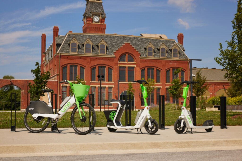 Three Lime vehicles—two electric scooters and a bike—stand ready on a Chicago street, patiently awaiting passengers amidst the bustling urban landscape.