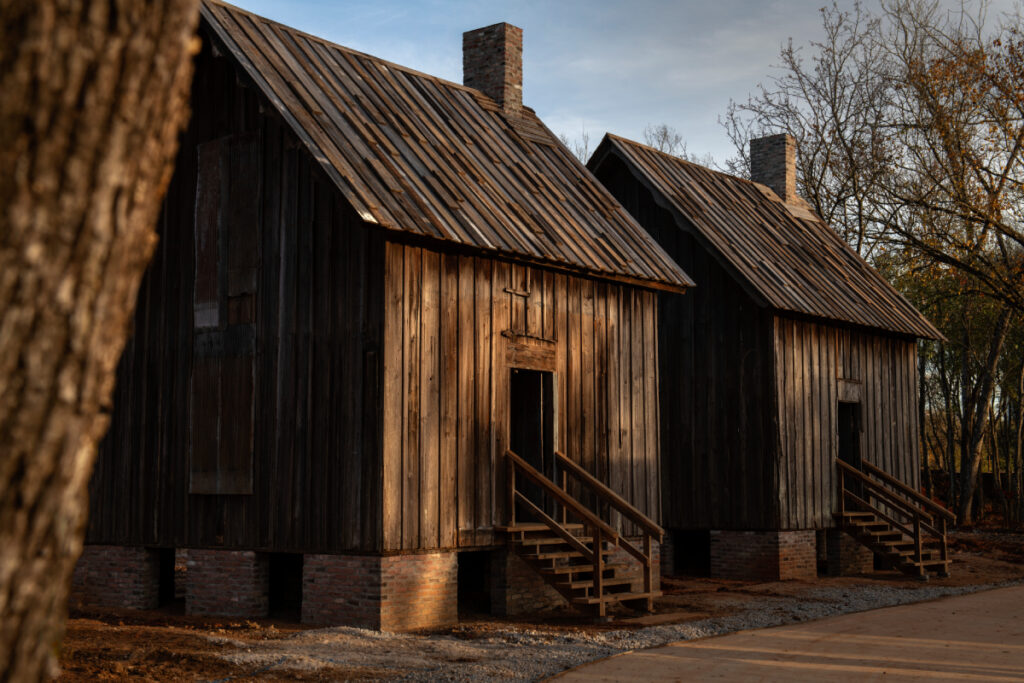 An image portrays two weathered wooden houses, former homes of Black slaves, bearing the visible marks of time's passage, serving as relics of a painful past.