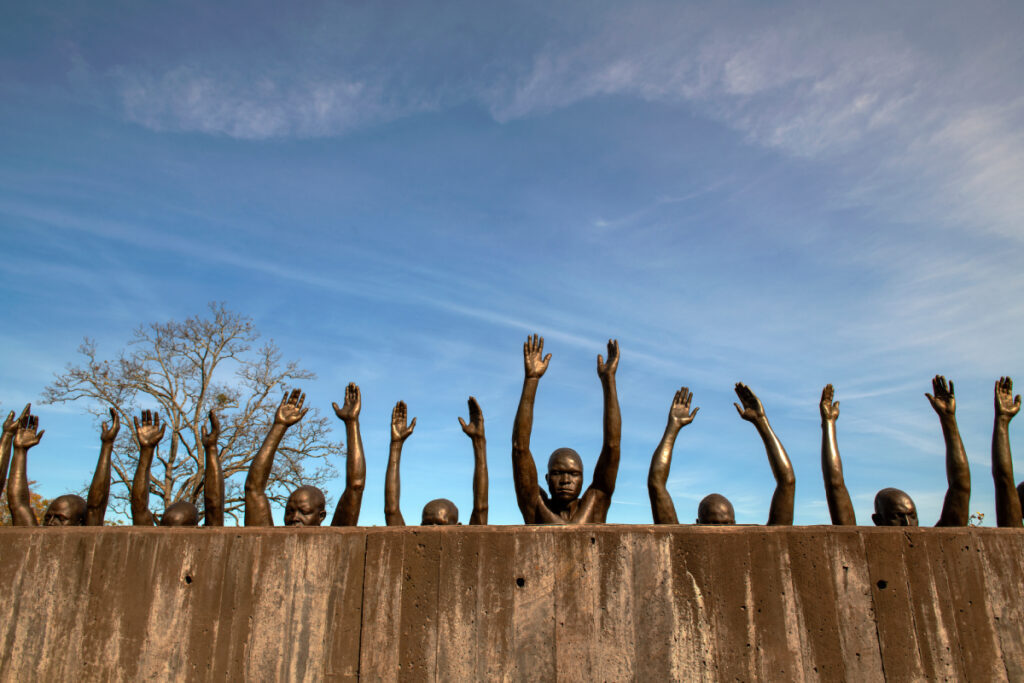 Image capturing the powerful sculpture of multiple black slaves rising behind a concrete wall, their hands lifted in the air, photo by Robert Rausch.