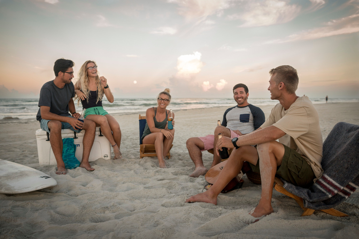 A color photograph by Scott van Osdol of a group of friends hanging out on the beach at dusk. 
