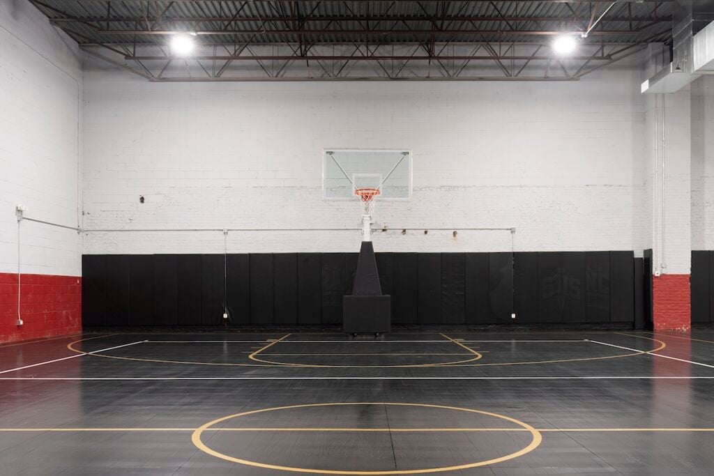 Backplate image of a basketball gym interior, with black floor and white and red painted cinderblock walls, by NYC-based Architecture photographer Emily Andrews.