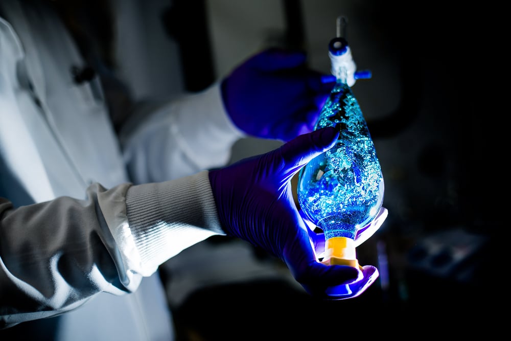 Photo of a scientist holding a bright blue liquid in a glass container, taken by Scott Gable for Chimerix, showcasing science/technology photography. 