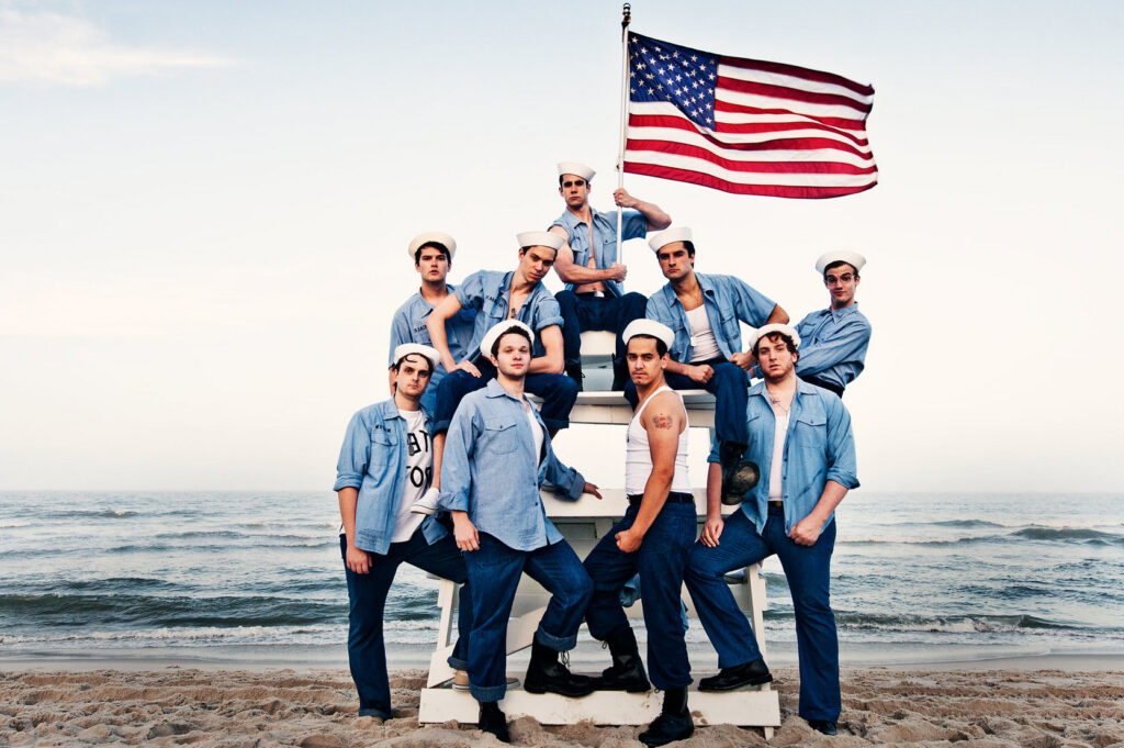 Image of men dressed casually in navy attire holding an American flag on the beach, taken by Starboard & Port.