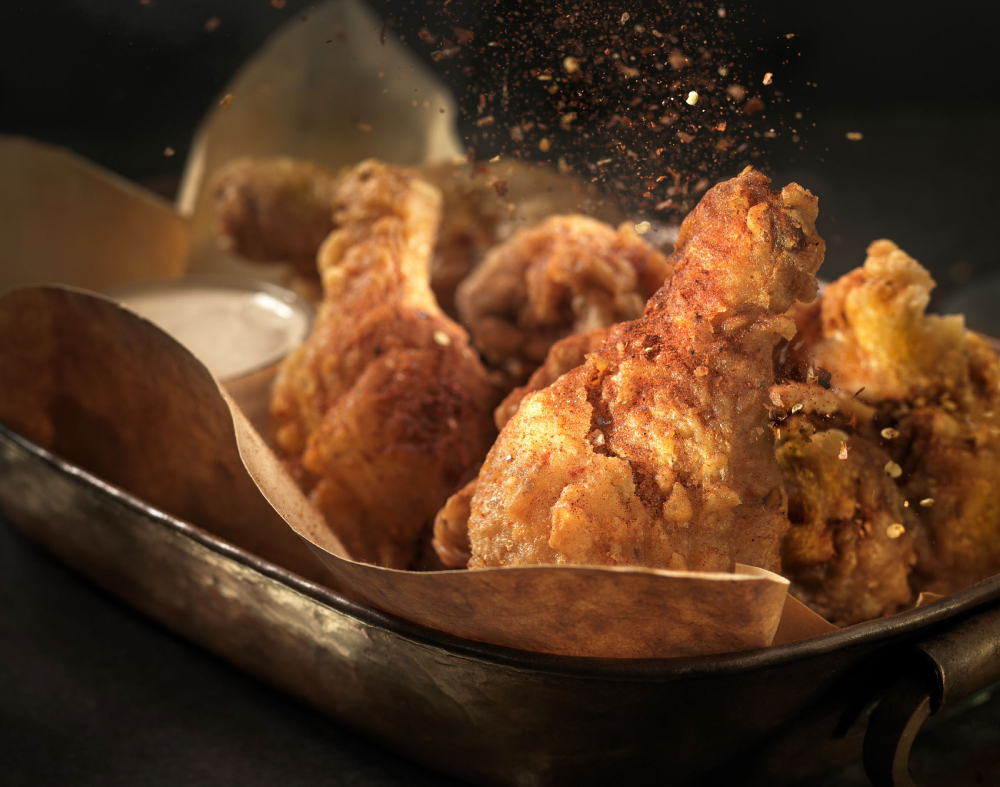 Photo by Steve Hansen of fried chicken sitting in a hot pan as seasoning is being put on.
