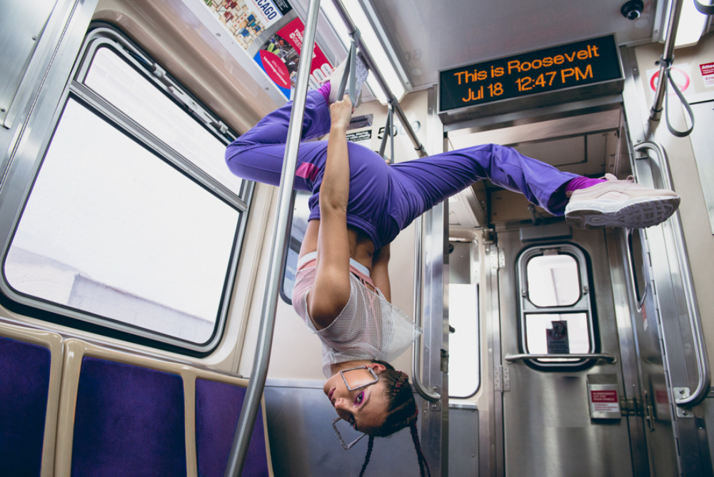 Photo by Zoe Rain of a girl hanging upside down in a subway car wearing activewear.